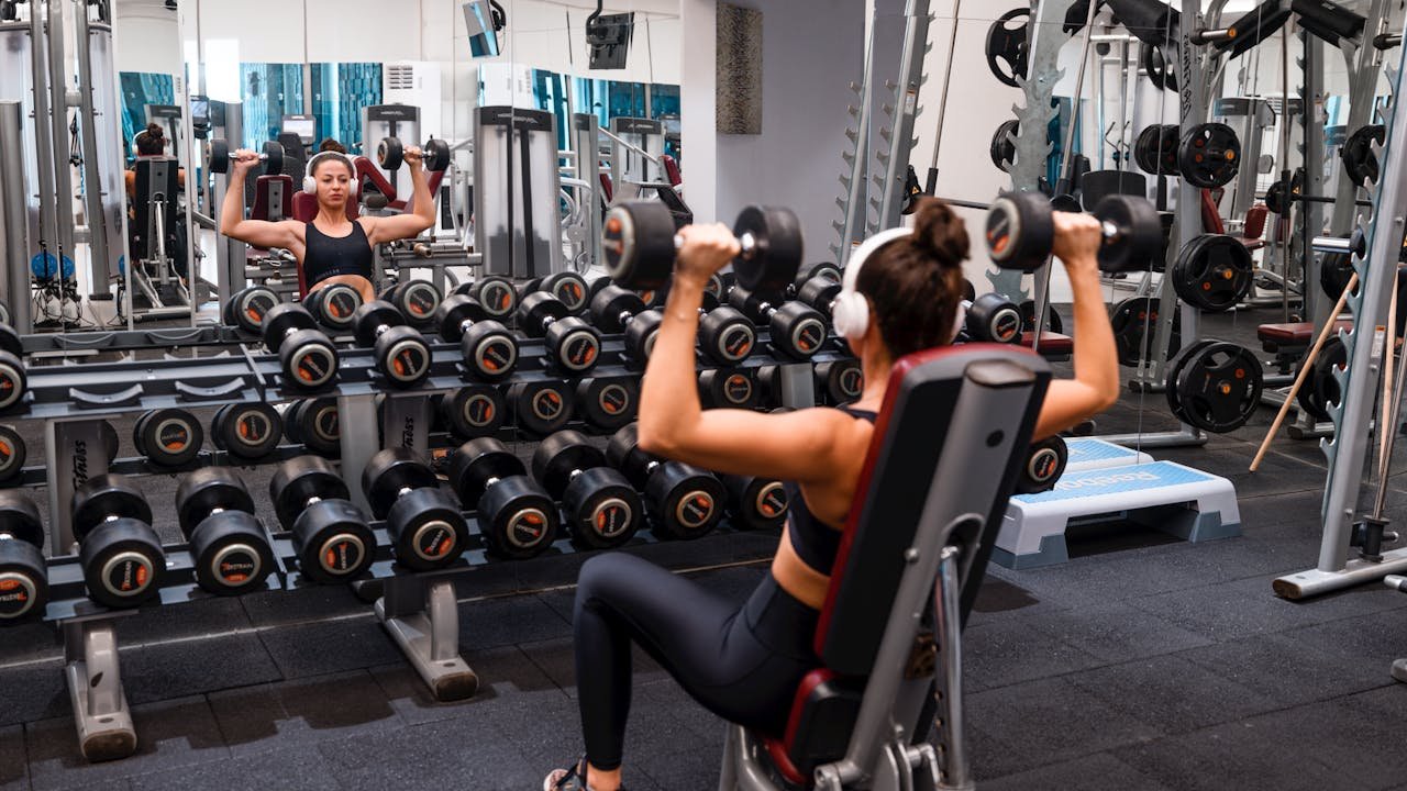 Offerings Woman exercising in the gym lifting dumbbells with headphones on for a strength-building workout.